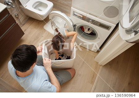 Father and daughter sorting clothes from a laundry basket for washing 136590964