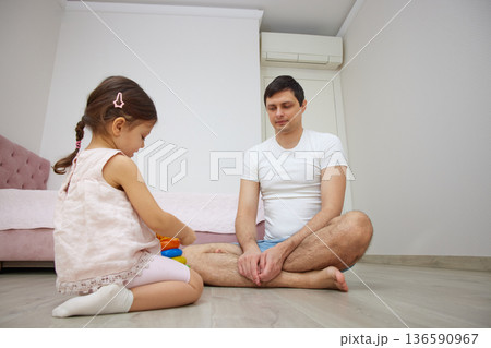 Father and daughter playing with colorful stacking toys on the wooden floor at home Father and daughter playing with colorful stacking toys on the wooden floor at home 136590967