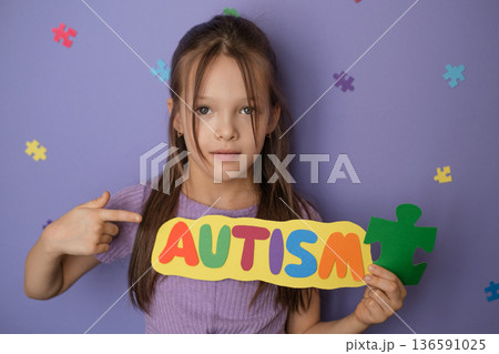 Portrait of young girl holding colorful Autism sign with puzzle piece symbol against purple background. Concept of autism awareness, neurodiversity acceptance, social support for child Portrait of young girl holding colorful Autism sign with puzzle piece symbol against purple background. Concept of autism awareness, neurodiversity acceptance, social support for child 136591025