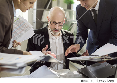 Overwhelmed manager surrounded by coworkers and paperwork, stress and burnout 136591266