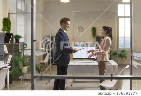 Businessman and businesswoman discussing strategy with tablet in modern glass office Businessman and businesswoman discussing strategy with tablet in modern glass office 136591277