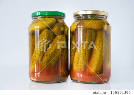 Glass jars with salted pickled cucumbers in tomato sauce, homemade preservation on a light background 136591396