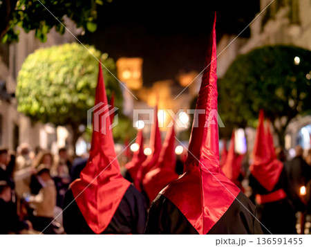 Many nazarenos with red hoods walking in procession 136591455