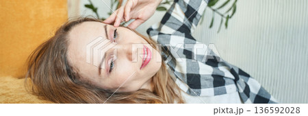 Caucasian female relaxing in checkered shirt on yellow couch, smiling Caucasian female relaxing in checkered shirt on yellow couch, smiling 136592028