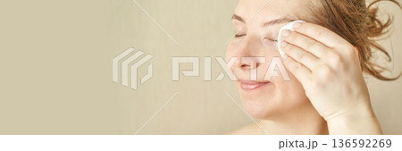 Caucasian female removing makeup with cotton pad, smiling, young adult Caucasian female removing makeup with cotton pad, smiling, young adult 136592269