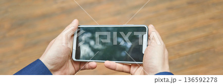 Person holding smartphone with blurred screen on wooden background Person holding smartphone with blurred screen on wooden background 136592278