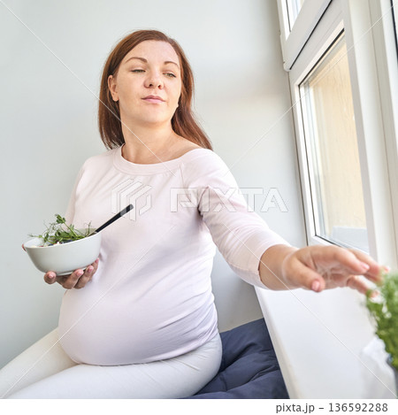 Pregnant caucasian female relaxing by window eating salad in comfortable home 136592288