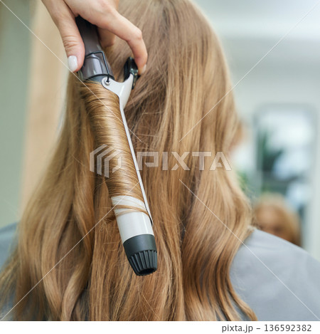 Young caucasian woman getting long brown hair styled with curling iron in salon Young caucasian woman getting long brown hair styled with curling iron in salon 136592382