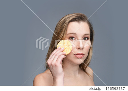 Young caucasian female with facial sponge for skincare routine on gray 136592387