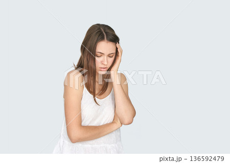 Young caucasian female appearing stressed or unwell with hand on head in white Young caucasian female appearing stressed or unwell with hand on head in white 136592479