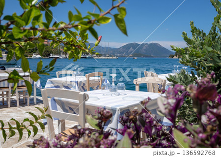 Served tables in a Greek tavern in Vathy Harbor, Meganisi island, Ionian Sea, Greece during the summer tourist season. Horizontal. Served tables in a Greek tavern in Vathy Harbor, Meganisi island, Ionian Sea, Greece during the summer tourist season. Horizontal. 136592768