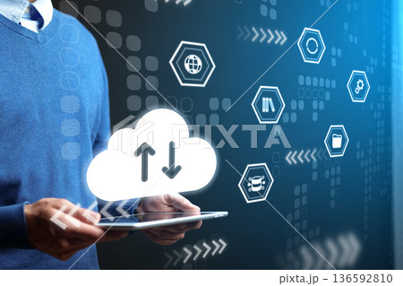 Hands holding tablet with cloud icons showing data transfer in a tech workspace during day 136592810