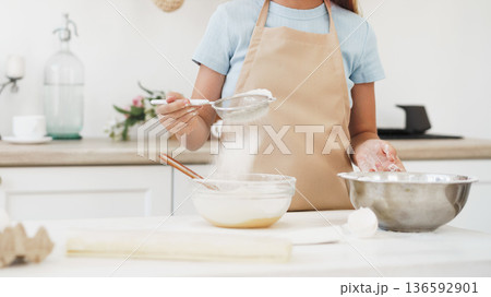 Person sifting flour into a mixing bowl in a kitchen during daytime cooking activity Person sifting flour into a mixing bowl in a kitchen during daytime cooking activity 136592901