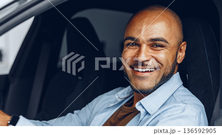 Man smiles while sitting in a car at a parking area during the day Man smiles while sitting in a car at a parking area during the day 136592905