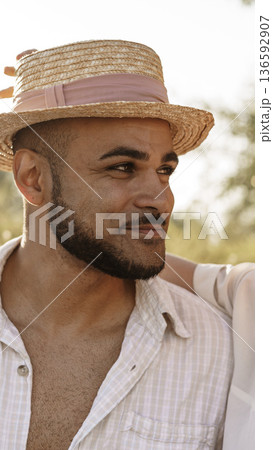 Man wears hat and smiles while standing outdoors with a friend during sunny weather Man wears hat and smiles while standing outdoors with a friend during sunny weather 136592907