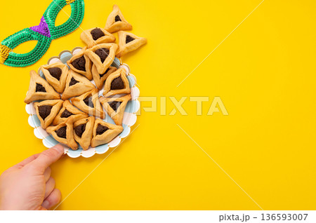 Hands holding Hamantaschen cookie isolate on yellow background. Hands holding Hamantaschen cookie isolate on yellow background. 136593007