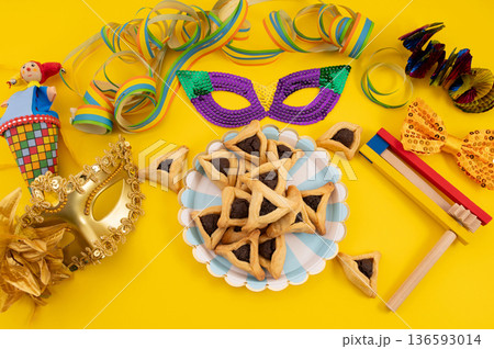 Frame made of carnival mask, rattles, Hamantaschen cookies and decor for Purim holiday on yellow background. Frame made of carnival mask, rattles, Hamantaschen cookies and decor for Purim holiday on yellow background. 136593014