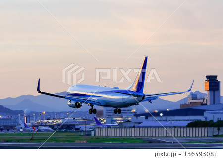 夕焼けの滑走路へ着陸する旅客機 136593081