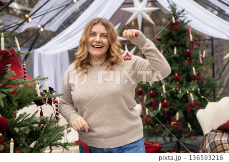 Young woman in sweater decorating Christmas tree at home and smiling. Winter time and holidays. Celebration banner 136593216