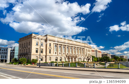 Des Moines Historic City Hall in Iowa. Historic Beaux-Arts architecture features a limestone facade with columns and arched windows near the river under a blue sky 136594099