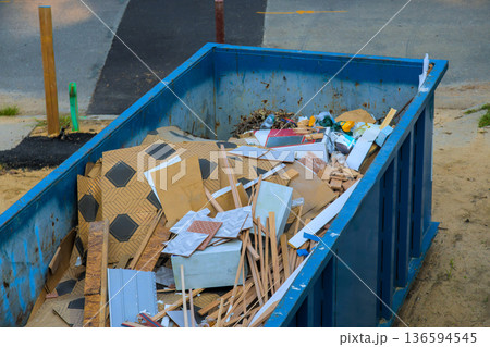 Construction debris fills large blue waste dumpster near street Construction debris fills large blue waste dumpster near street 136594545