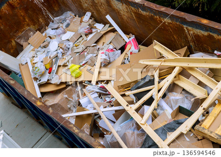 Construction site waste is piled in large dumpster under renovation home Construction site waste is piled in large dumpster under renovation home 136594546