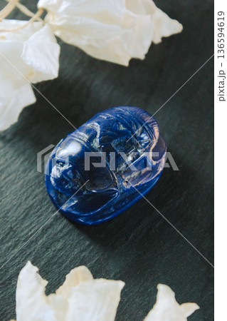 Beautiful lapis lazuli scarab beetle with dried white petals on a dark slate stone, ancient charm. 136594619
