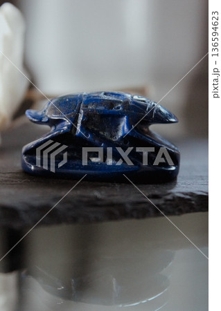 Side view of a blue lapis lazuli scarab beetle figurine on a dark stone surface, ancient talisman. Side view of a blue lapis lazuli scarab beetle figurine on a dark stone surface, ancient talisman. 136594623