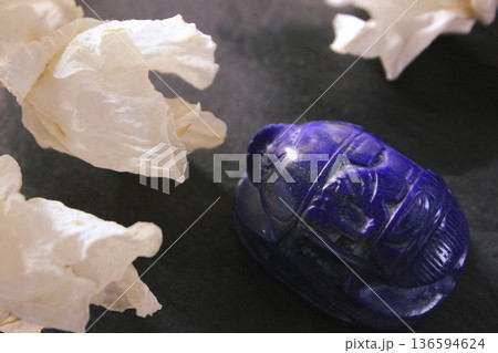Lapis lazuli scarab beetle carving with dried white flowers on dark stone background, ancient symbol. Lapis lazuli scarab beetle carving with dried white flowers on dark stone background, ancient symbol. 136594624