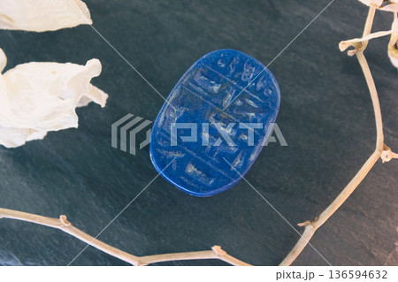 Lapis lazuli scarab base with engraved ancient egyptian hieroglyphs on dark stone with white petals. 136594632