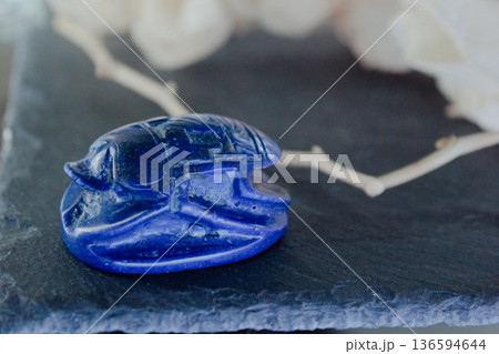 Lapis lazuli scarab beetle carving on dark slate stone with decorative dry branches, ancient amulet. 136594644