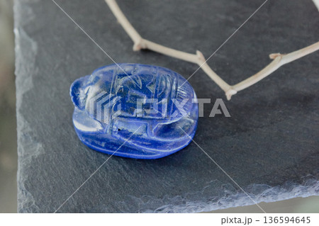 Lapis lazuli scarab beetle carving on dark slate stone with decorative dry branches, ancient amulet. 136594645