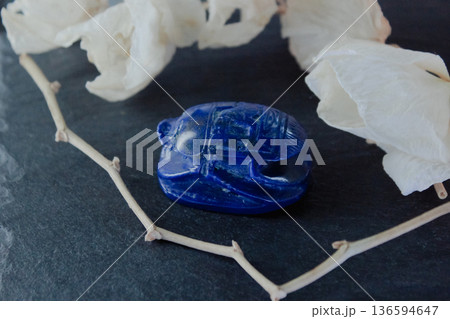 Lapis lazuli scarab beetle on dark slate surrounded by white petals and dry branches, sacred symbol. Lapis lazuli scarab beetle on dark slate surrounded by white petals and dry branches, sacred symbol. 136594647
