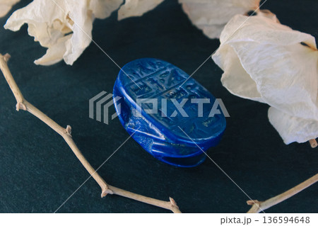 Lapis lazuli scarab base with engraved ancient egyptian hieroglyphs on dark stone with white petals. Lapis lazuli scarab base with engraved ancient egyptian hieroglyphs on dark stone with white petals. 136594648