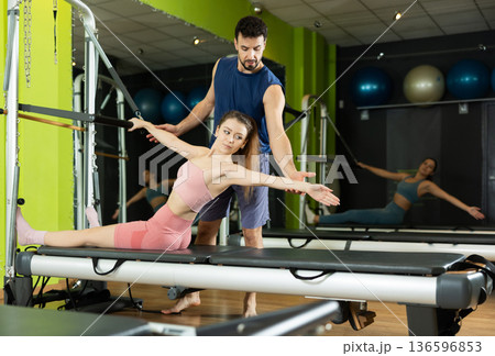 Male trainer guiding girl during abdominal press exercise on reformer 136596853