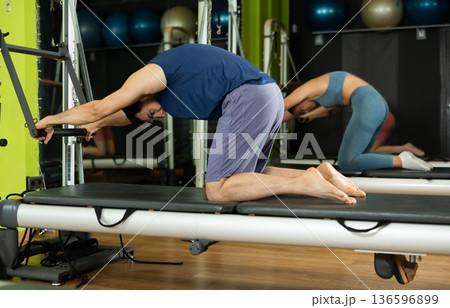 Young man performing pilates reformer spine stretch during group class 136596899
