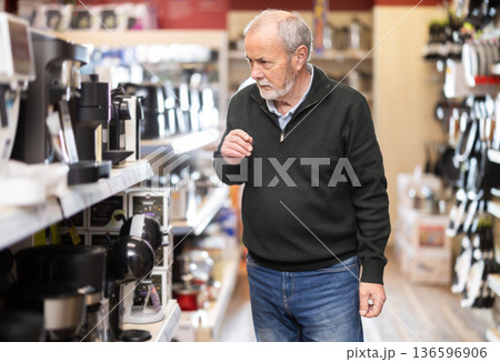 Elderly man chooses coffee machine in hypermarket Elderly man chooses coffee machine in hypermarket 136596906