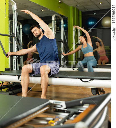 Young man performing pilates reformer stretch during group class Young man performing pilates reformer stretch during group class 136596913