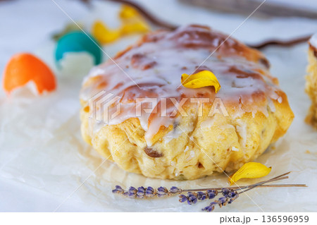 Close up of glazed easter bread on crinkled parchment with colorful cracked egg shells and a lavender sprig. Soft focus Close up of glazed easter bread on crinkled parchment with colorful cracked egg shells and a lavender sprig. Soft focus 136596959