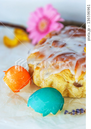 Closeup still life of glazed easter bread with gerbera daisy and cracked  colorful easter egg shells on parchment paper. Soft focus 136596961