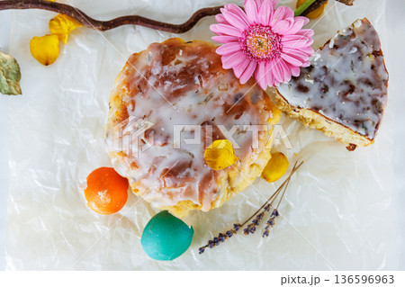 Overhead still life of  glazed easter bread with gerbera daisy and cracked  colorful easter egg shells on parchment paper. Soft focus 136596963
