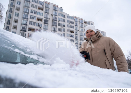 Man Clearing Snow from Car in Winter Cityscape 136597101