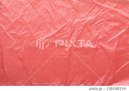 Abstract background of crumpled red plastic material symbolizing plastic waste pollution. Synthetic material texture, environmental issue, environmental concept 136598154