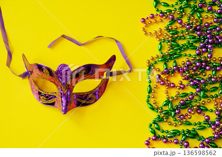 Multicolored beads and carnival mask on yellow background. Mardi Gras concept. Fat Tuesday symbol. Multicolored beads and carnival mask on yellow background. Mardi Gras concept. Fat Tuesday symbol. 136598562