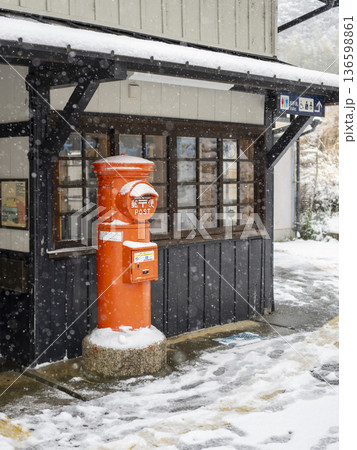 雪が降る駅に建つ丸ポスト 136598861