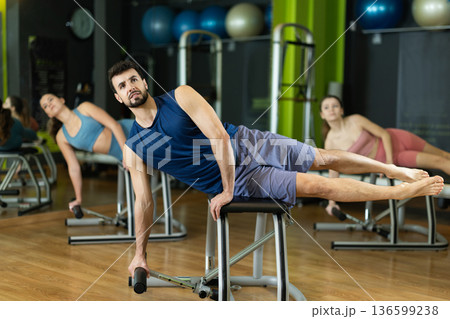 Young man performing side plank on pilates combo chair Young man performing side plank on pilates combo chair 136599238