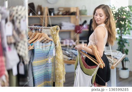 Happy woman chooses a set of clothes for the summer. Visitor to boutique examines new summer collection of clothes Happy woman chooses a set of clothes for the summer. Visitor to boutique examines new summer collection of clothes 136599285
