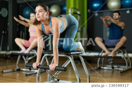 Young woman performing spinal stretch on pilates combo chair Young woman performing spinal stretch on pilates combo chair 136599317