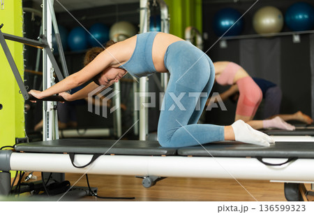 Young girl performing pilates reformer spine stretch during group class 136599323