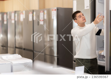Young man buyer examine fridge in detail before buying 136599367